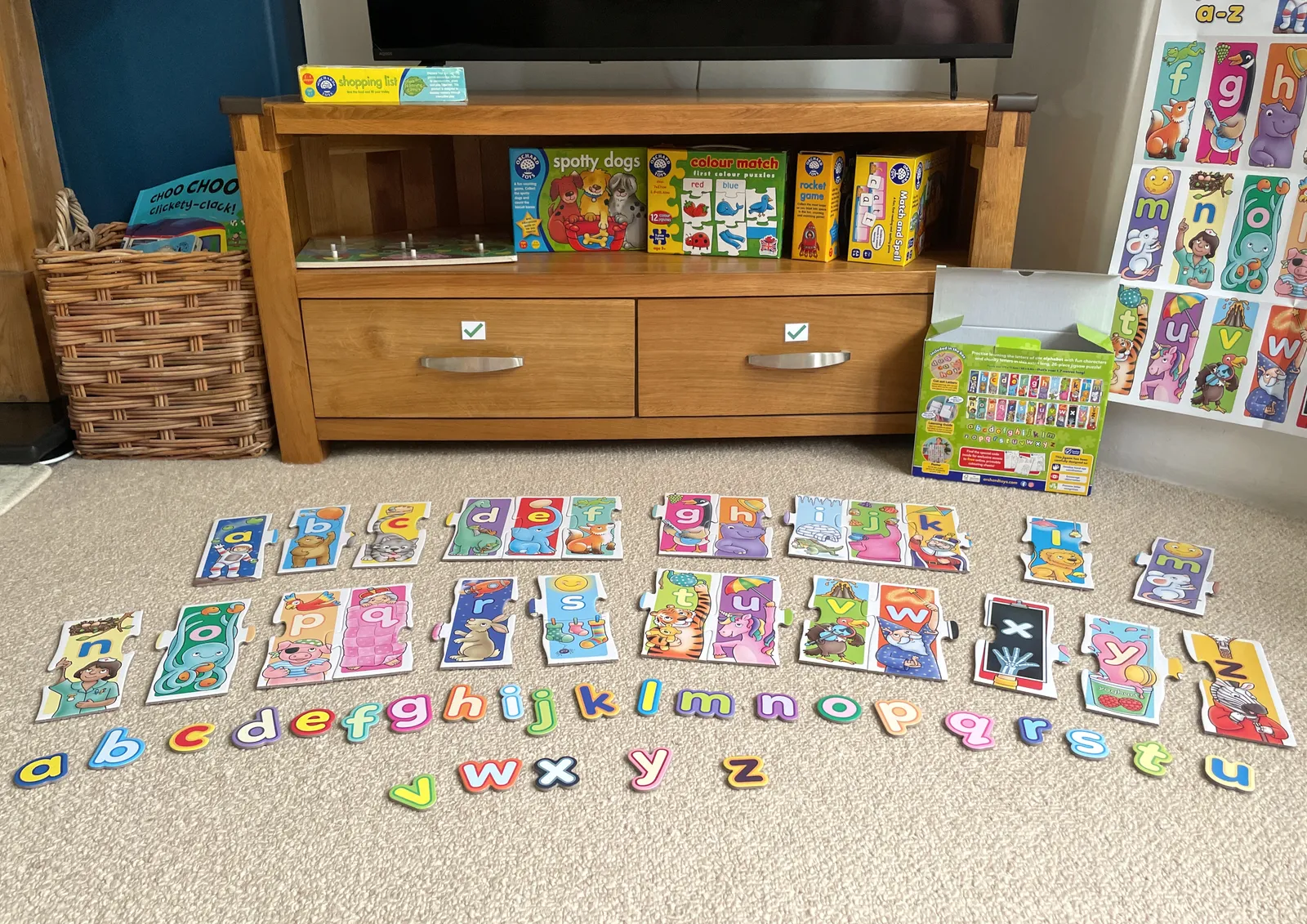 An alphabet puzzle on the carpet in front of a wooden drawer unit which has more boxed puzzles on display on the shelf above the drawers.