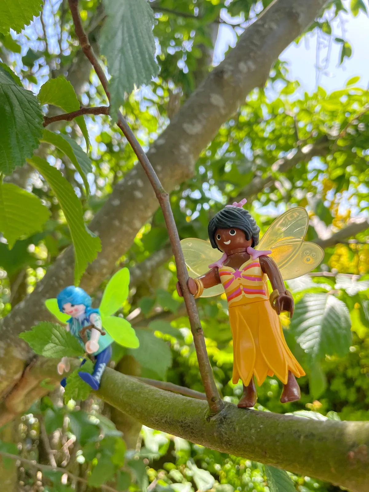 Two Playmobil fairies in the tree, one fairy wears blue clothes and has green wings, the other fairy is all in yellow.