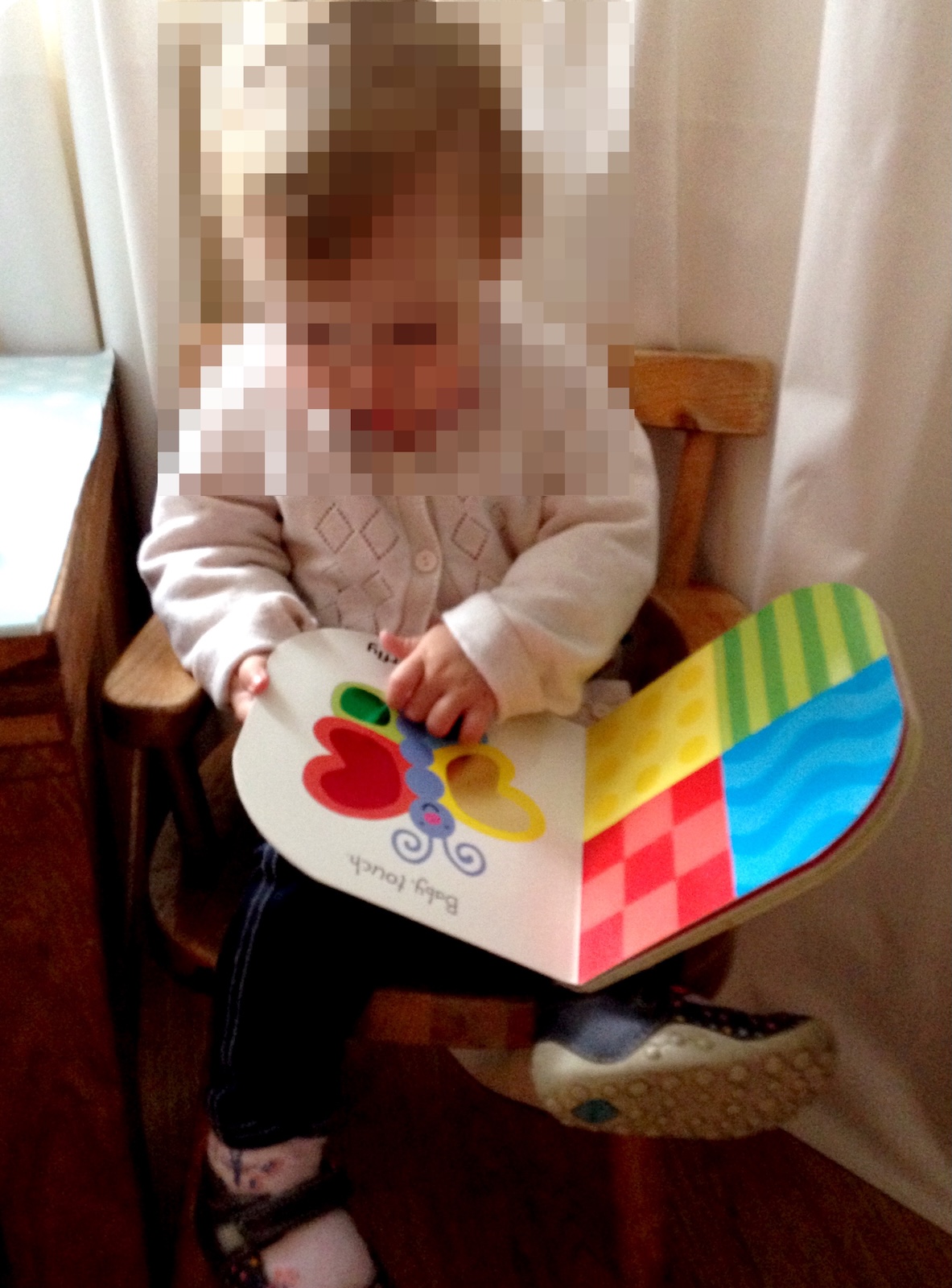A young child sitting in a wooden chair reading a colourful sensory touch-and-feel board book featuring a butterfly.